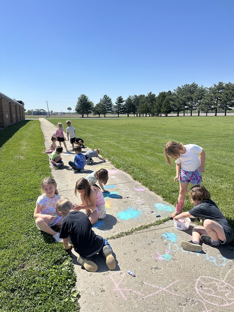 The students are sitting  on the sidewalk and playing with sidewalk chalk. 