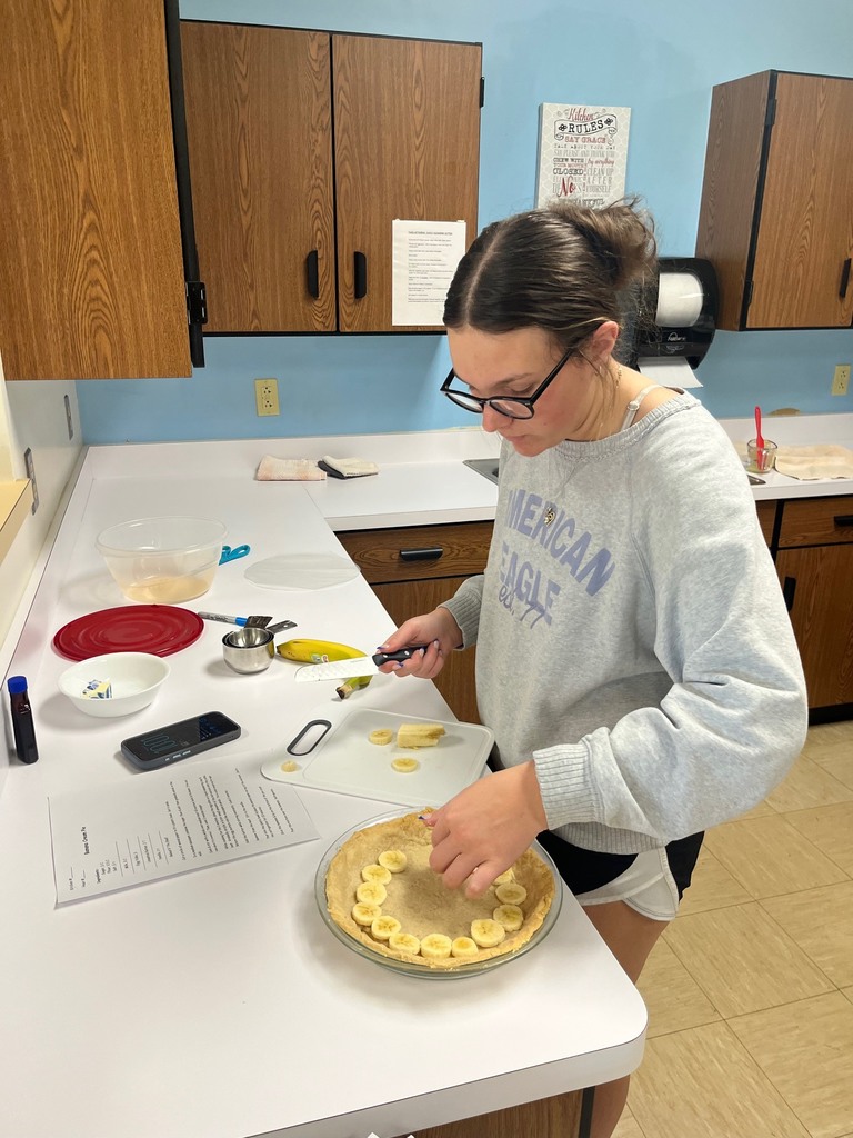 One student is cutting bananas and adding them to the pie crust. 