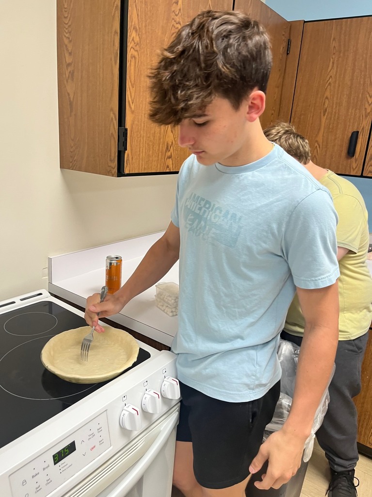 Ond student is poking holes in the dough with a fork. 