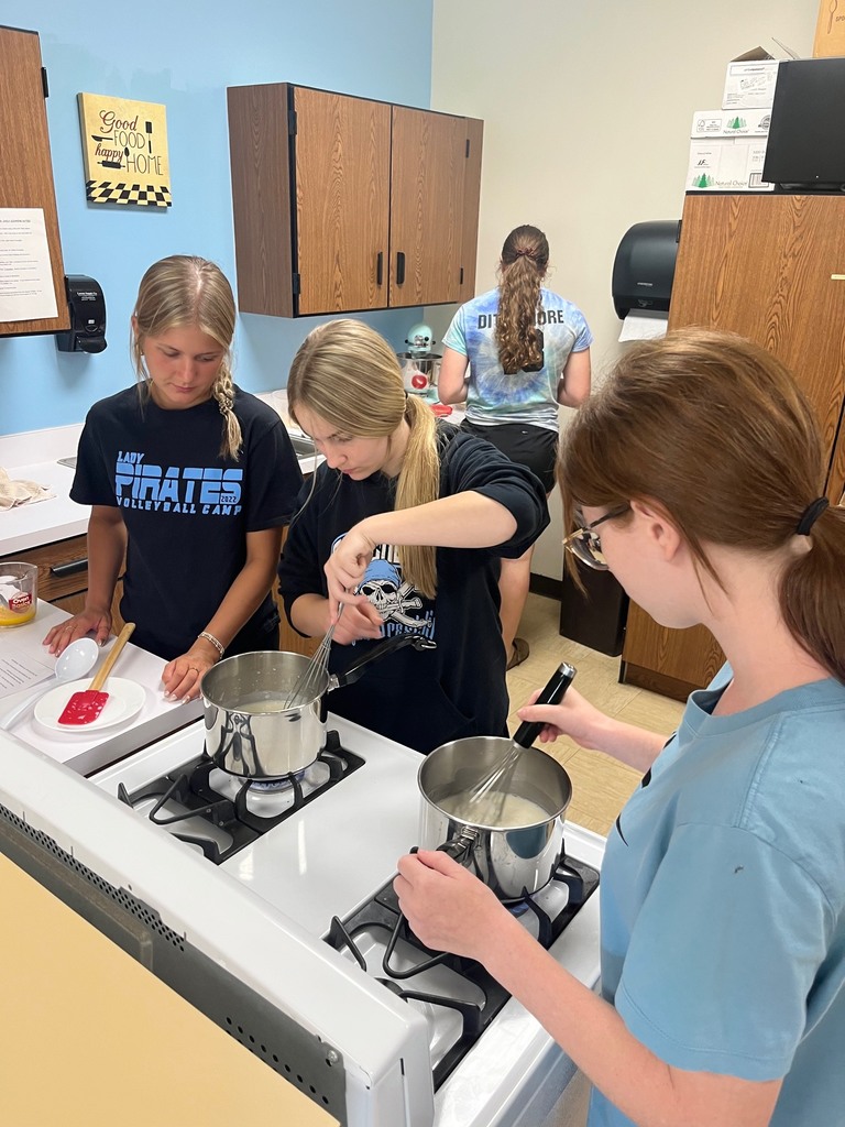 Two studetns are mixing ingredients in a sauce pan with a wisk. 