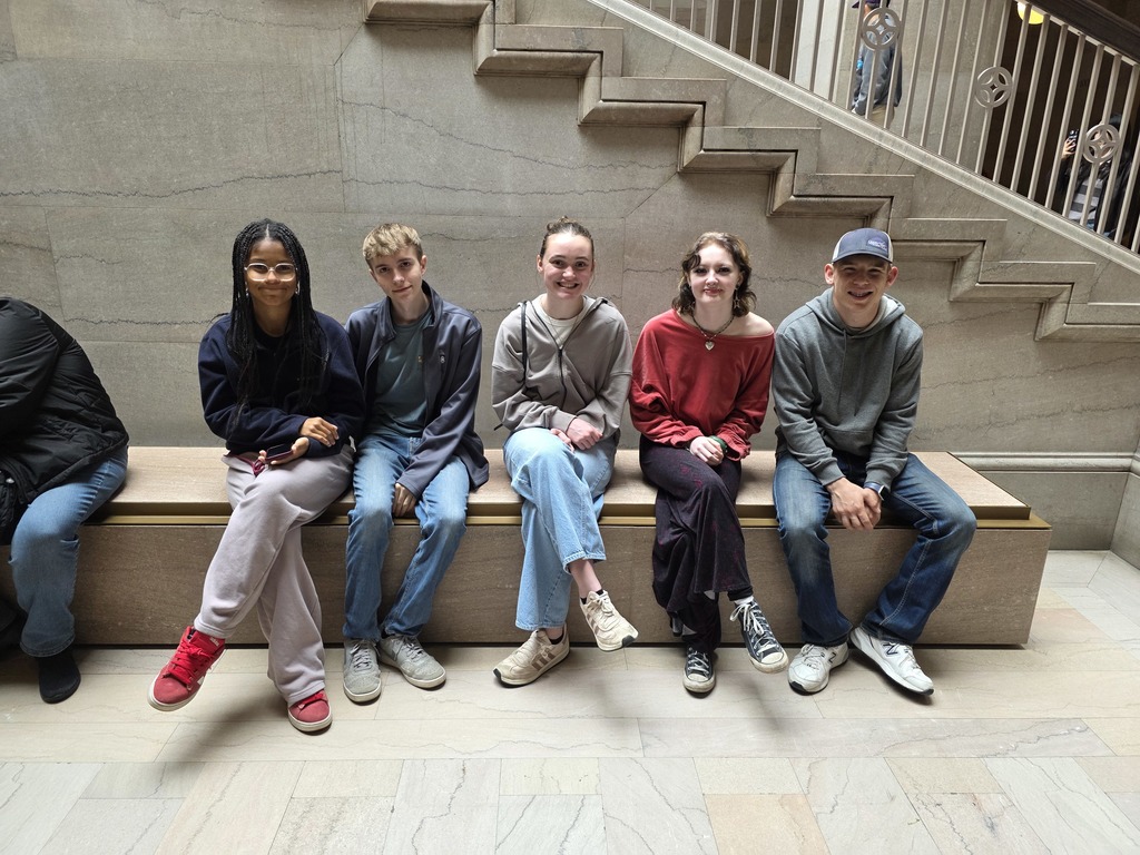 Five students are sitting on a bench in the  art museum. 