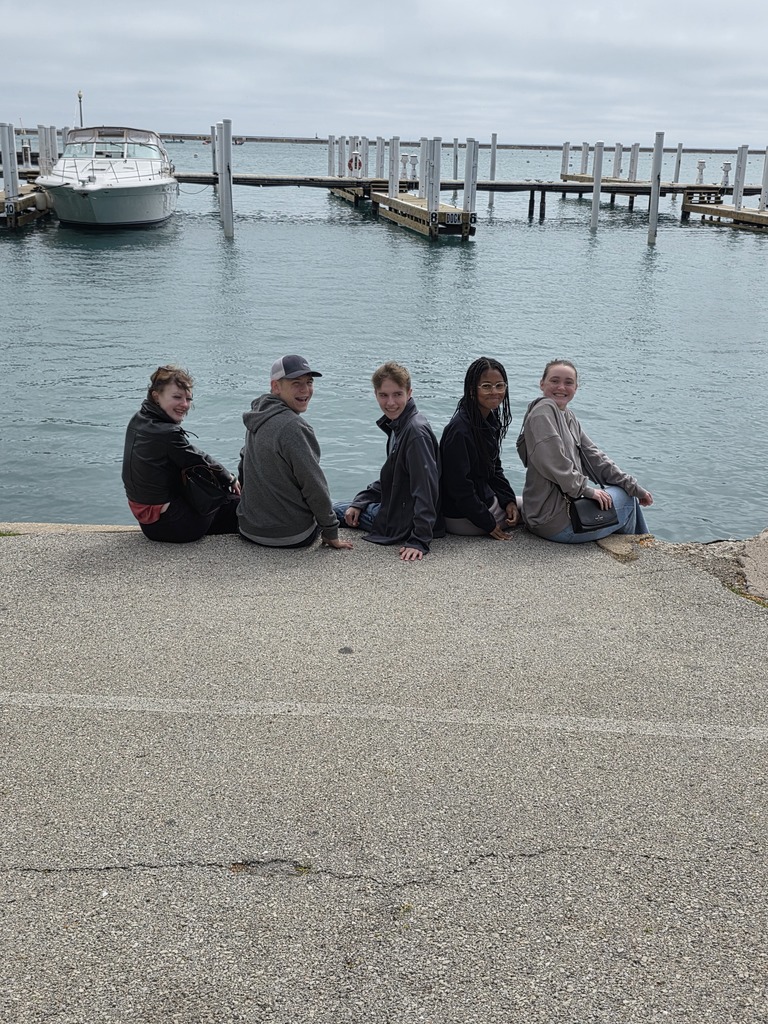 Five students are sitting at the end of the pier at Lake Michigan. 