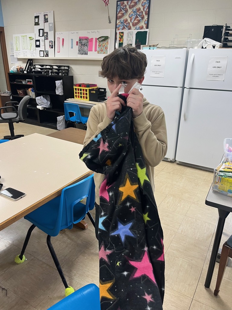A student is holding a pair pf PJs in front of the students face pointing to the pin that is on the PJs. 