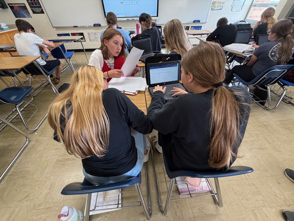 Three students are analyzing their graph on their laptop for trends. 