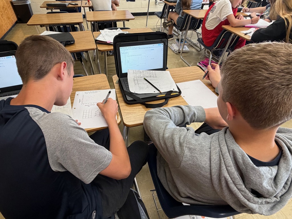 Two students are analyzing their graph on their laptop for trends. 