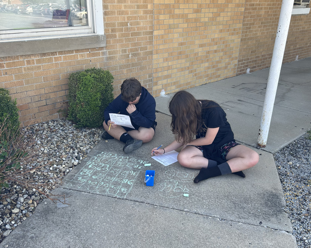 Two students are working on a Punnett square with sidewalk chalk.