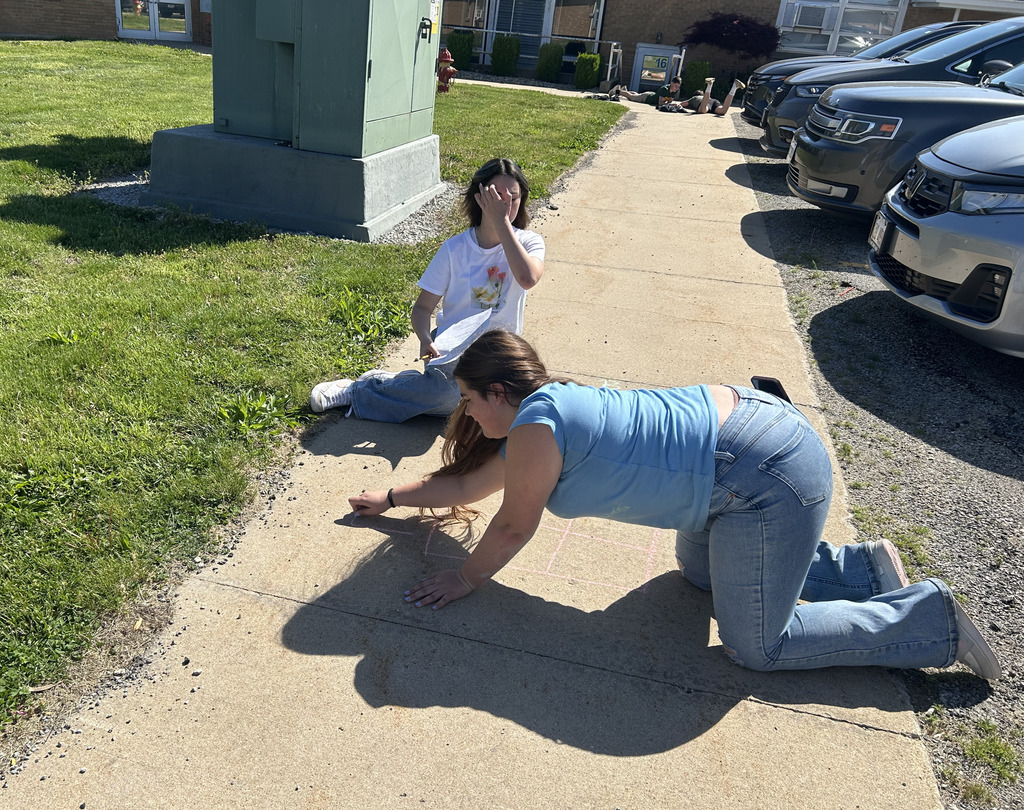 A student is working on a Punnett square with sidewalk chalk with the help of another student. 