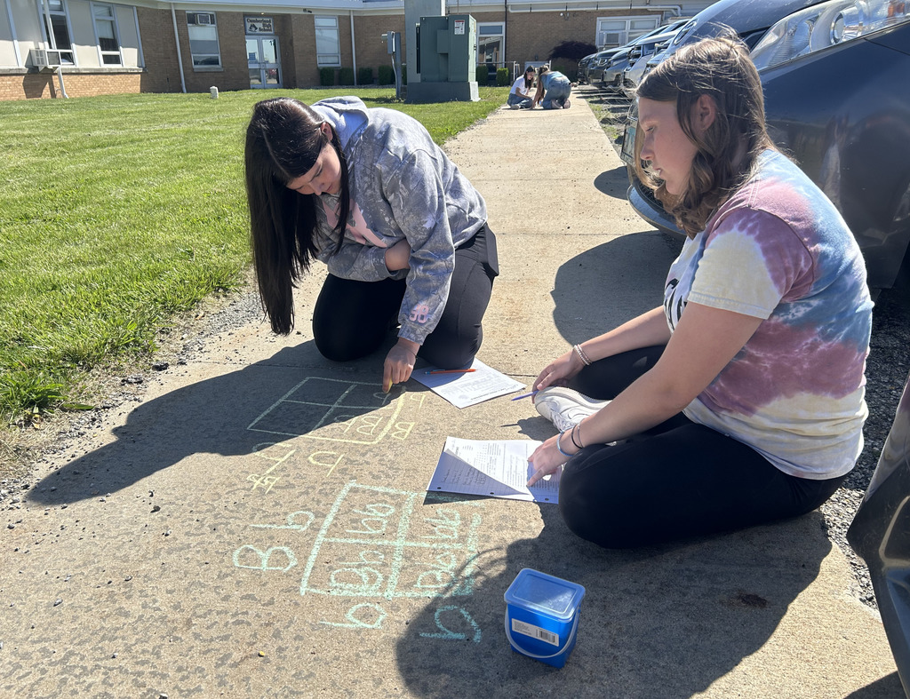 Two students are working on a Punnett square with sidewalk chalk.