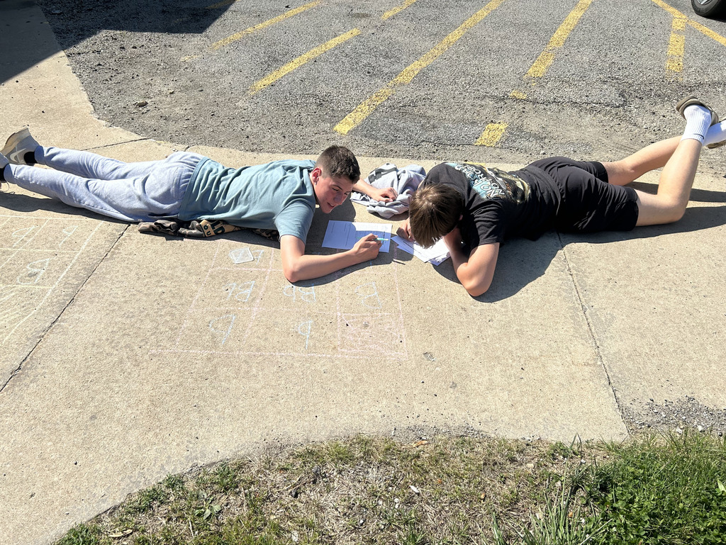 Two students are working on a Punnett square with sidewalk chalk.