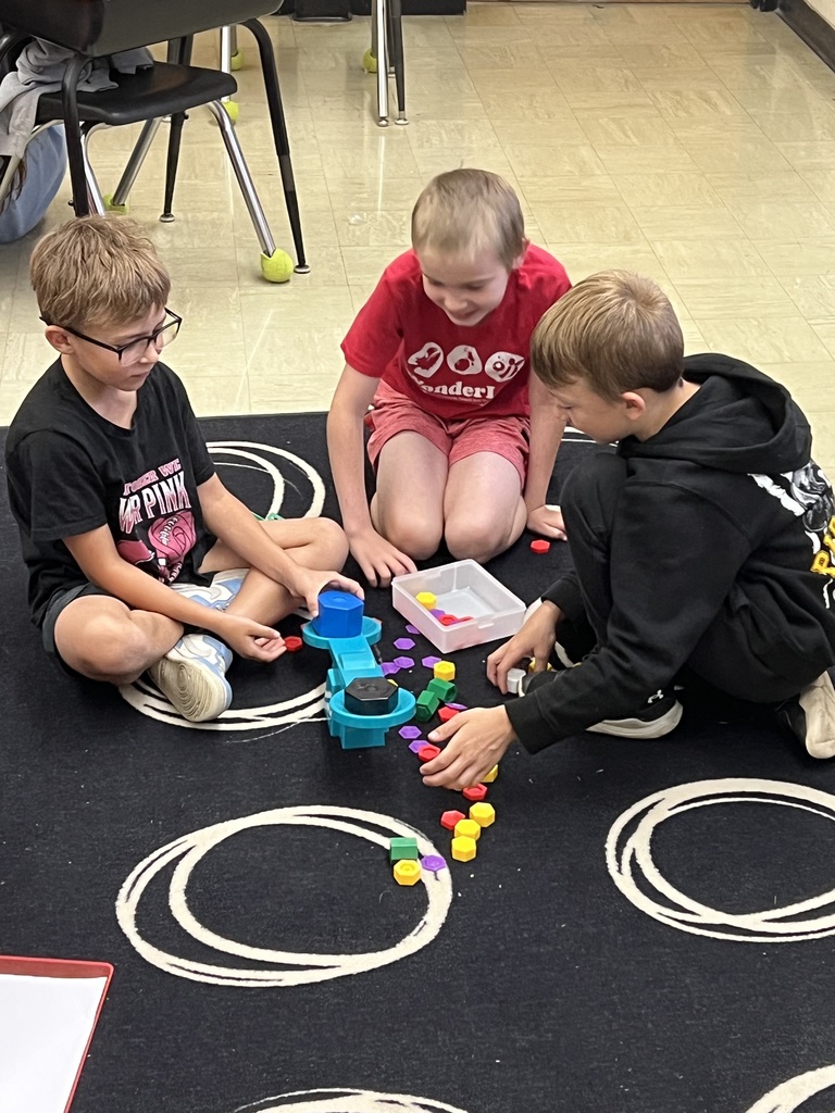 Three students are weighing objects to compare them on a scale. 