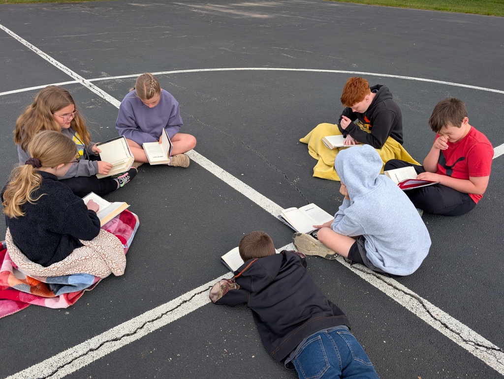 A group of seven students are reading their books together on the blacktop. 