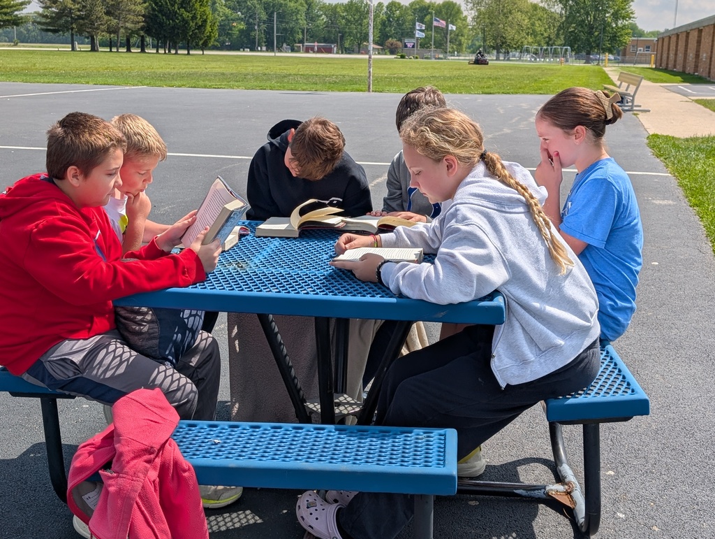 A group of six students are reading their books together at a picnic table. 