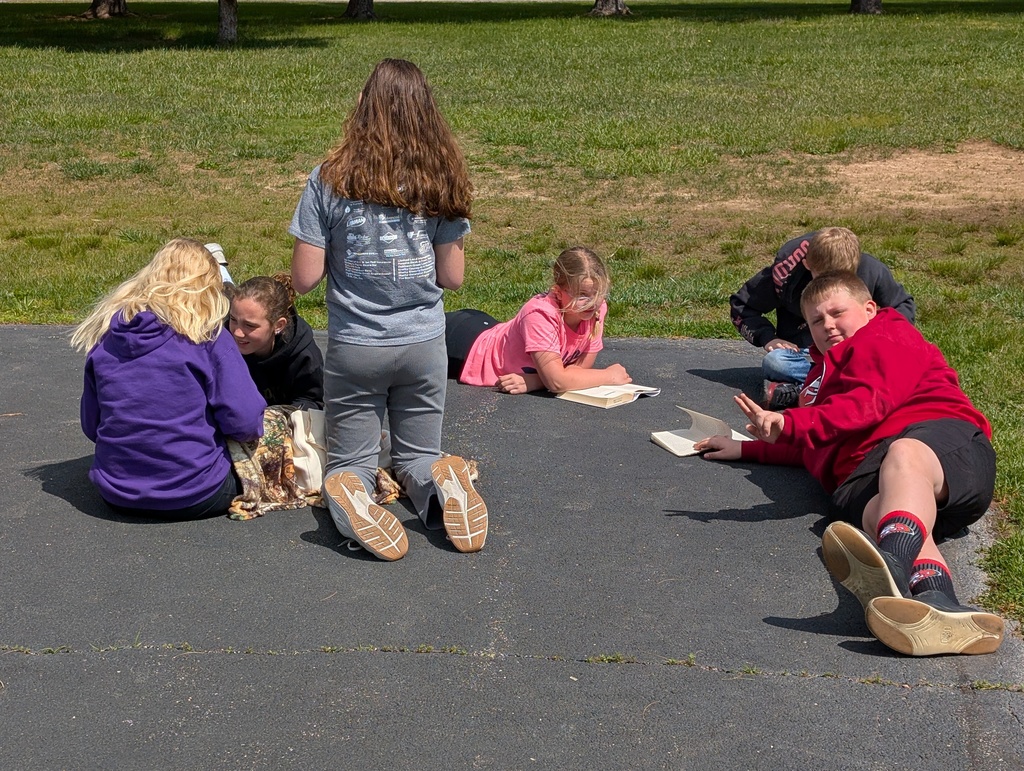 A group of six students are reading their books together on the blacktop. 