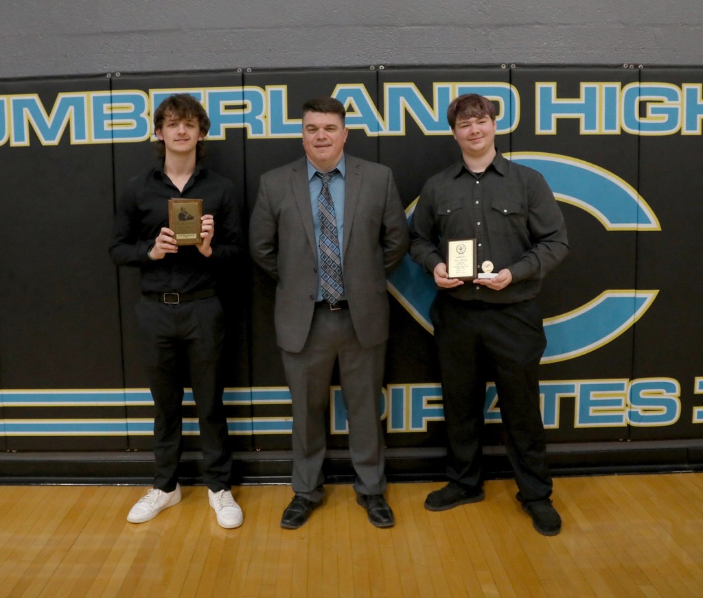 Two band award winners are standing with their instructor. They are holding their plaques. 