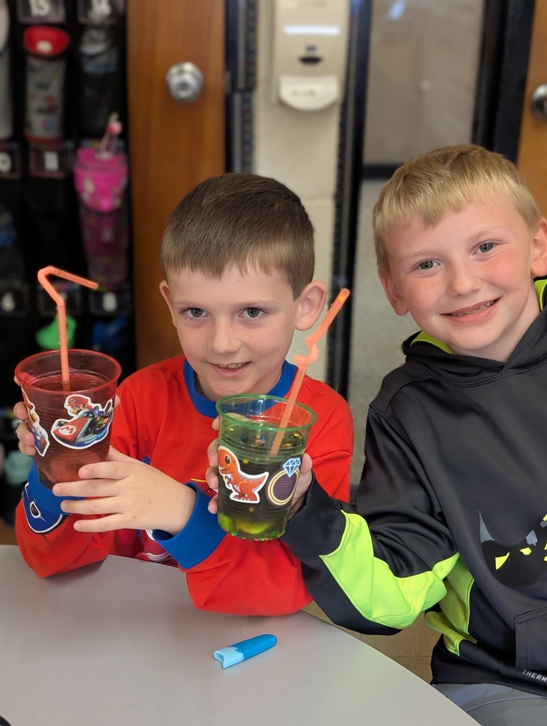 Two students are standing toghther holding up their cups with stickers and fancy staws. 
