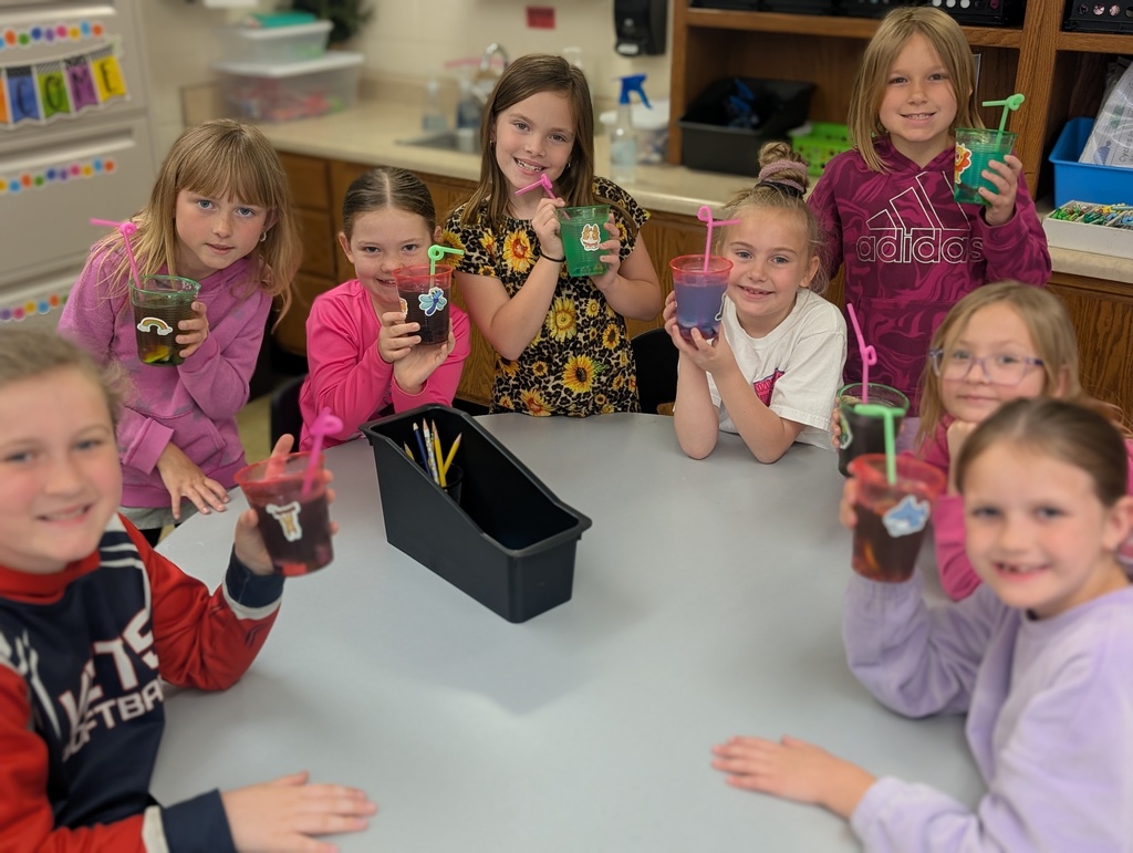 Eight students are around a table and showing their drink cups with stickers and fun straws. 