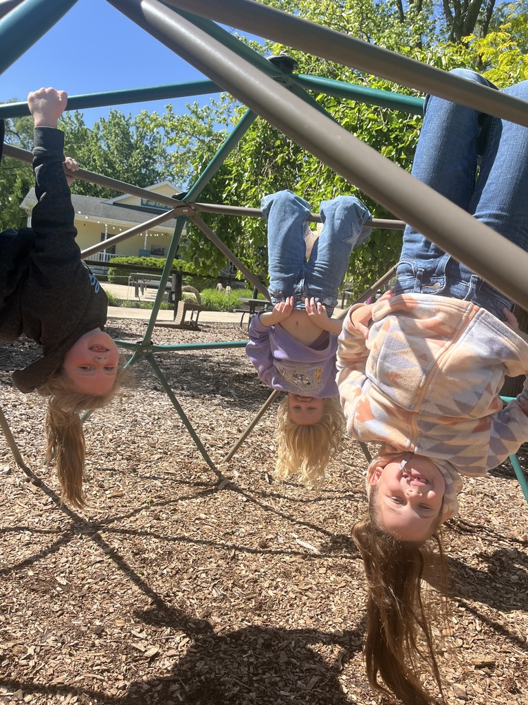 Three students are hanging upside down on the outside playground equiptment. 