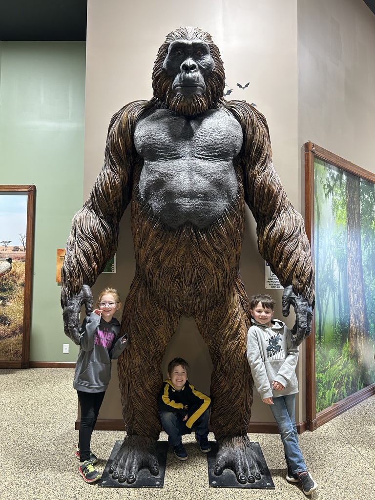 Three students are standing under a giant gorilla statue. 