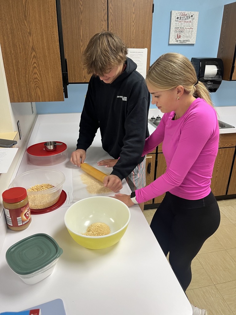 Two students are using a rolling pin to crush cereal.
