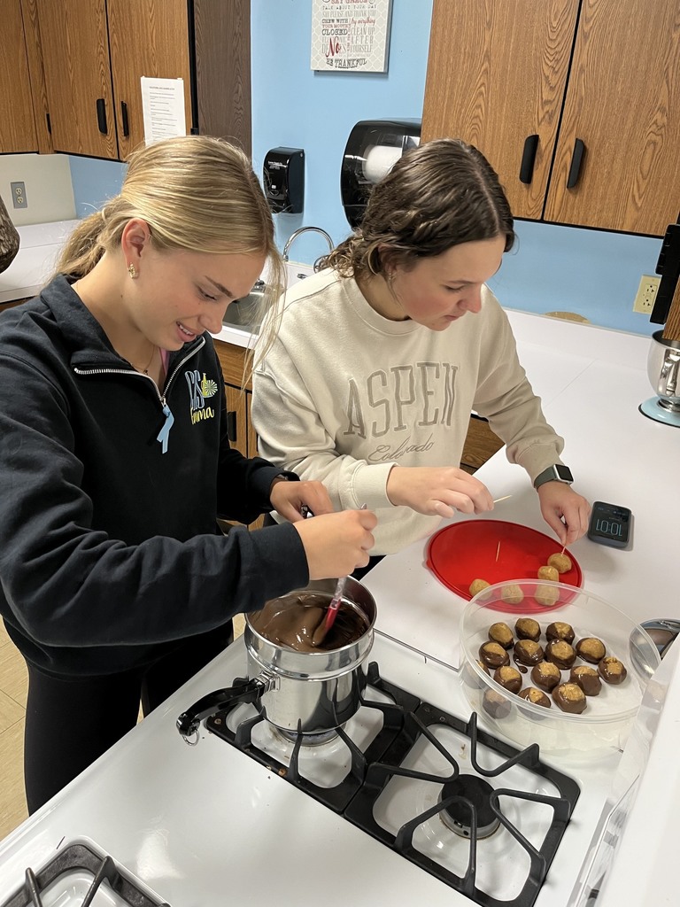 Two students are dipping balls into chocolate. 