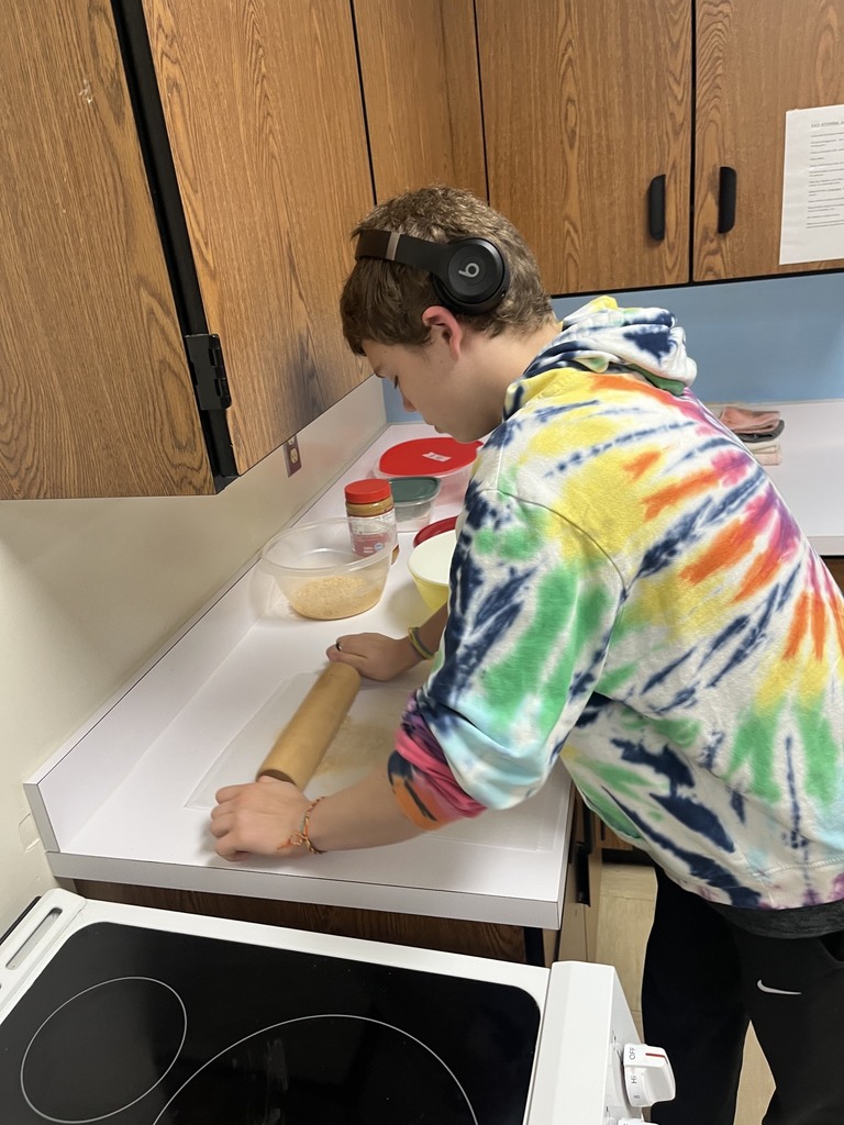 A student is using a rolling pin to crush cereal.