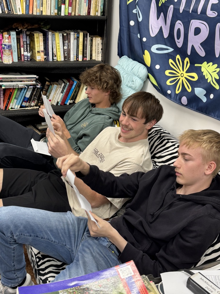 Three students are sitting on a couch reading their letters. 