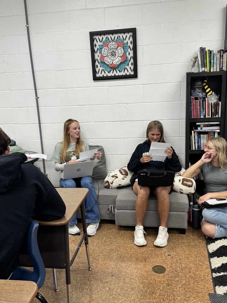Three students are sitting on chairs while reading their letters to each other. 