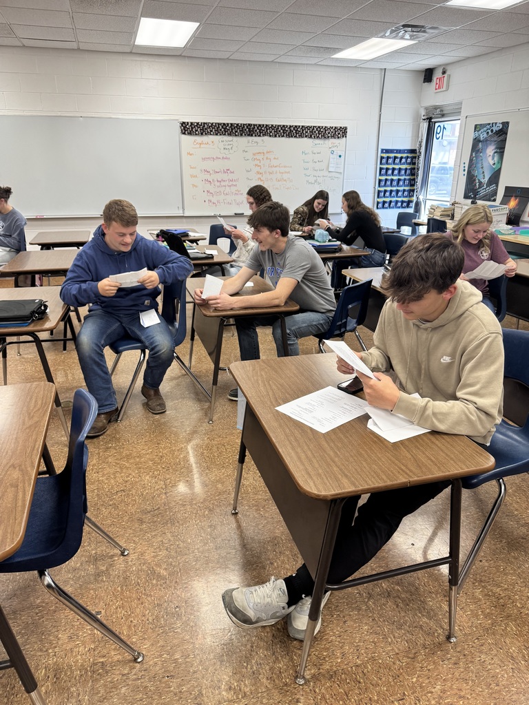 Students are sittingin desks reading their letters. 