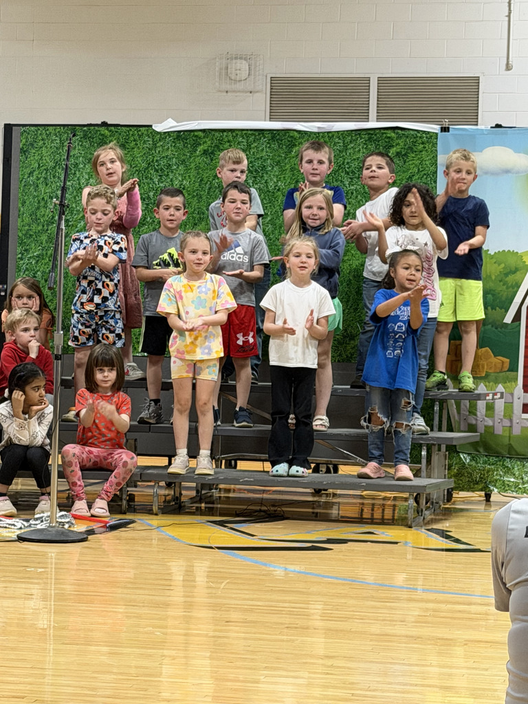 A group of students are standing on risers singing a song and clapping their hands. 