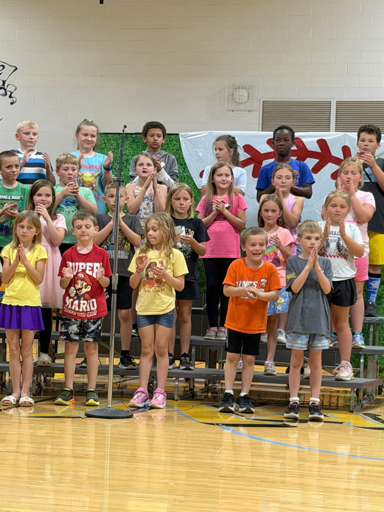 A group of students are standing on risers singing a song and clapping their hands. 