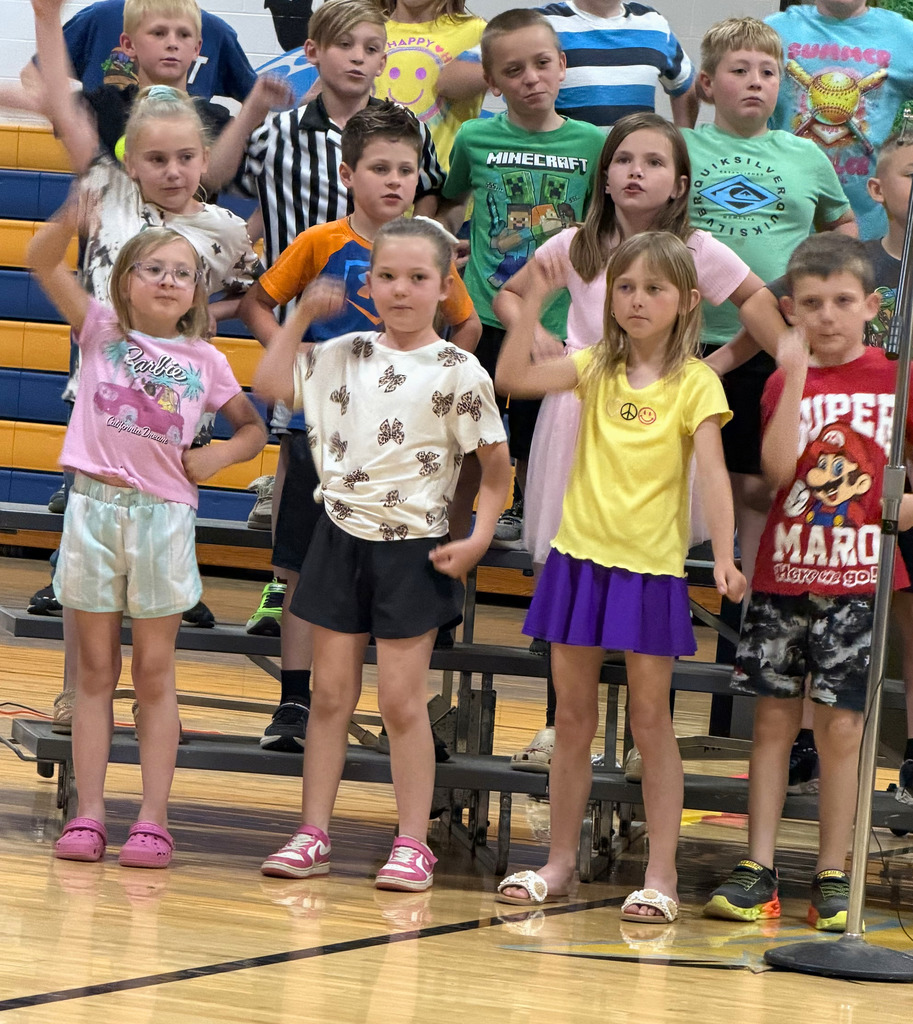 A group of students are standing on risers singing a song and raising their hand.
