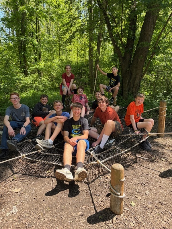 Pictured are ten members of the team sitting on a web-like net a foot above ground level. 