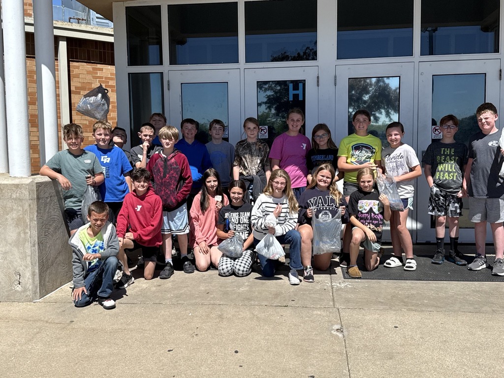 The class is gathered around the outer gym doors  with their bags of trash. 