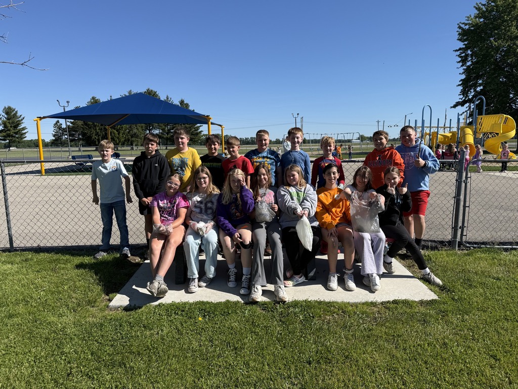 The class is gathered around a park bench with their bags of trash. 