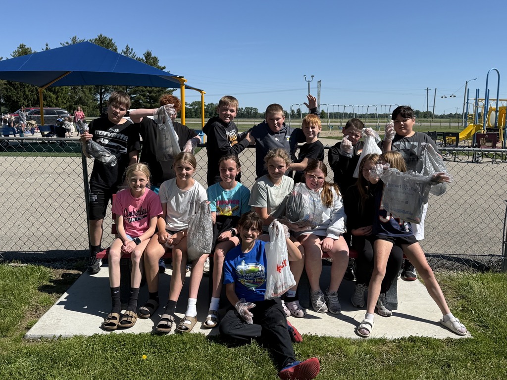 The class is gathered around a park bench with their bags of trash. 