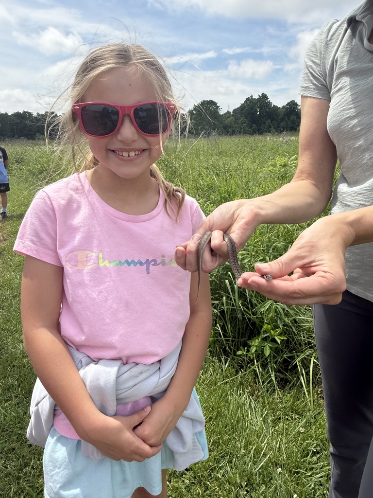 An adult is holding a snake and the student is looking at the camera. 