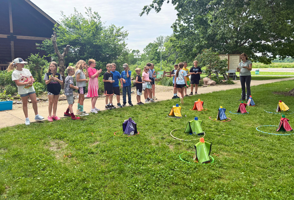 A class is playing a ring game. They are throwing rings around items in the grass. 