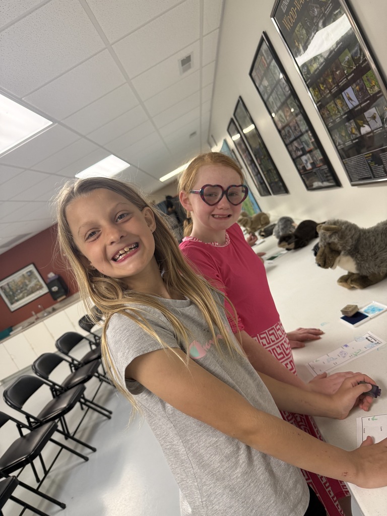 Two students are smiling at the camera. They are stamping their papers. 
