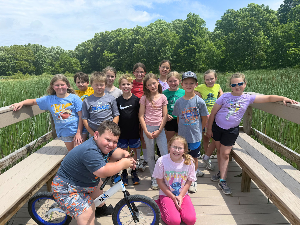 A class is standing at the end of a dock and posing for the camera. 