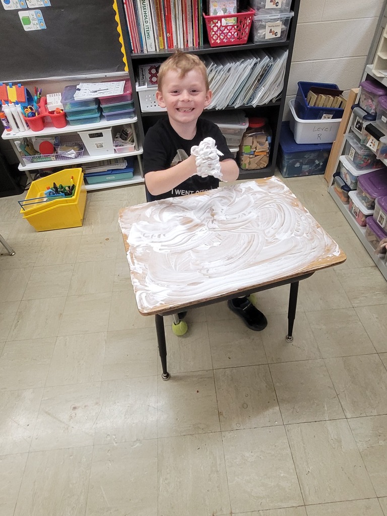 A student has shaving cream all over his desk. He has hands full, too. 