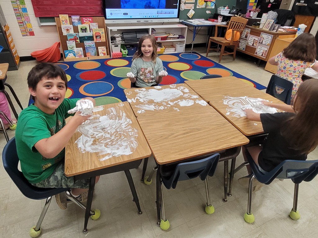 Two students hve shaving cream all over the desk. Their hands are  full, too. 