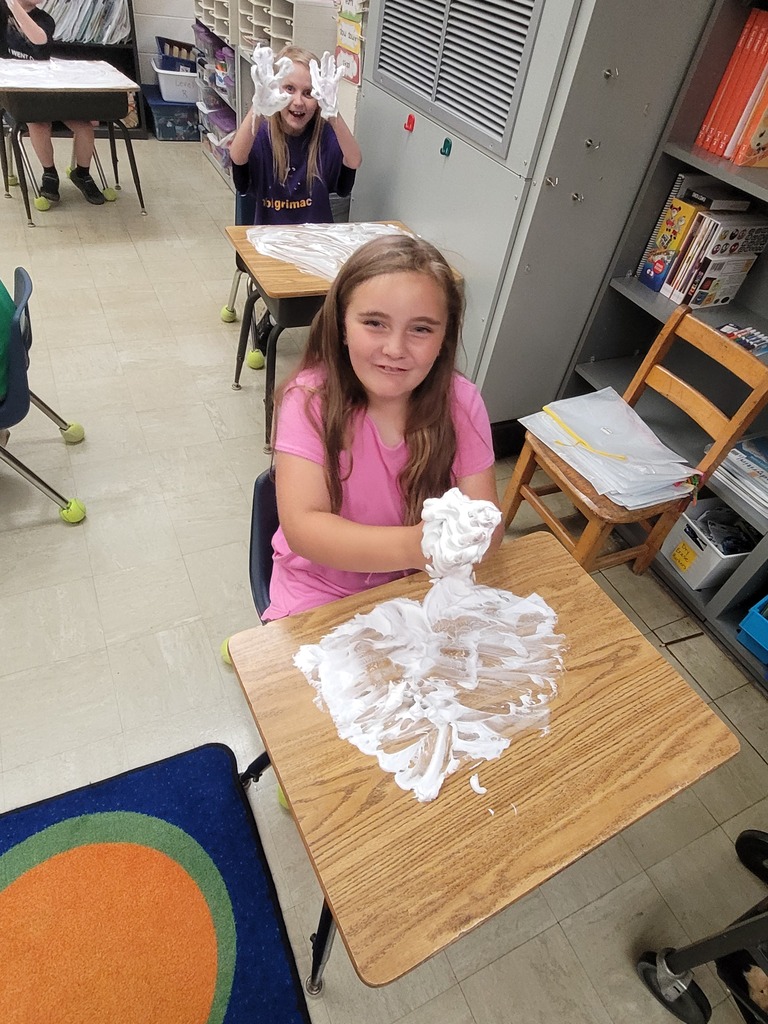 Two students hve shaving cream all over the desk. Their hands are  full, too. 