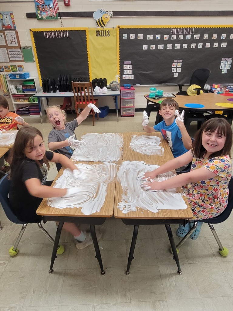 Four students hve shaving cream all over the desk. Their hands are  full, too. 