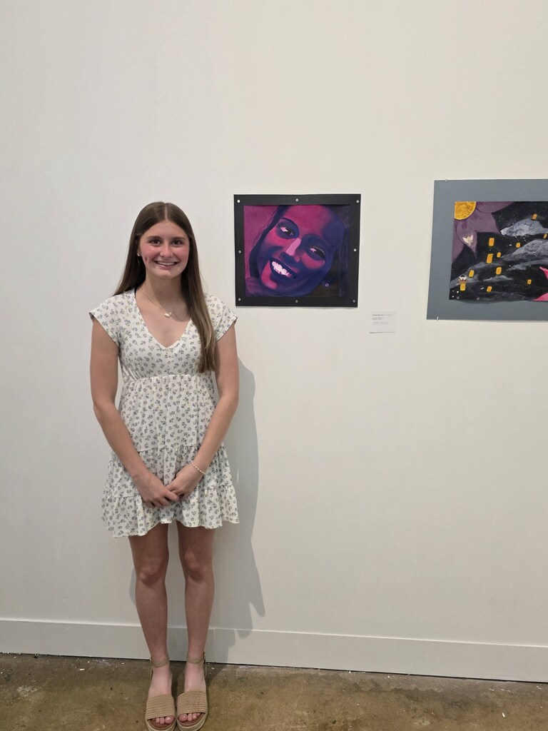 A student is standing next to their artwork,. 