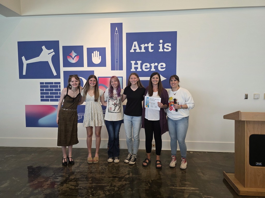 The group of art students and instructor are pictured on the stage with the emcee. 