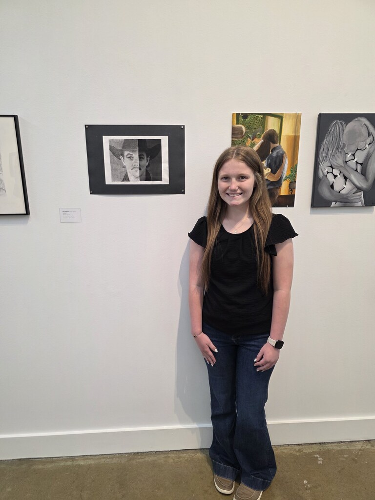 A student is standing next to their artwork,. 