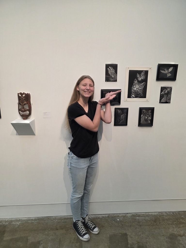 A student is standing next to their artwork,. 