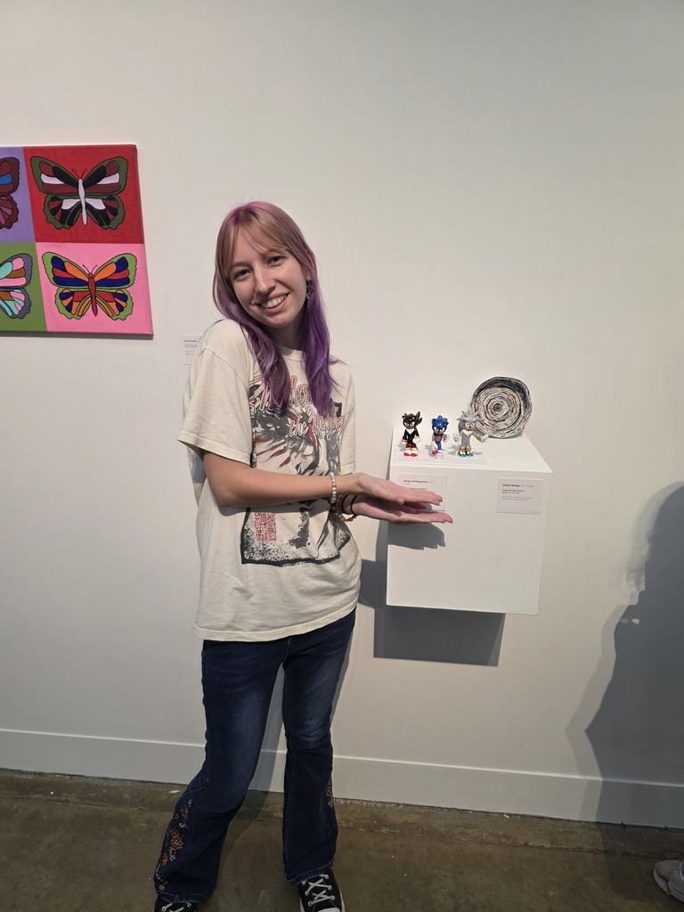 A student is standing next to their artwork,. 