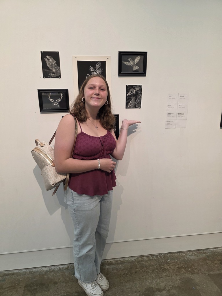 A student is standing next to their artwork,. 