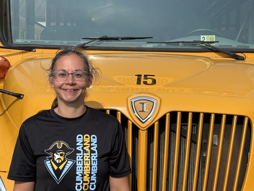 A bus driver is standing in front of their bus.